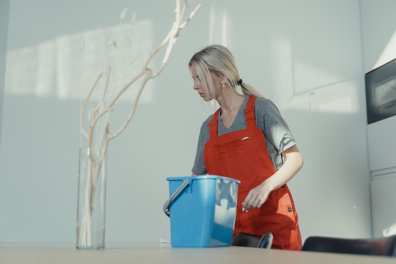 about-us-02 A woman in a red uniform cleans indoors with a blue bucket, ensuring a spotless environment.